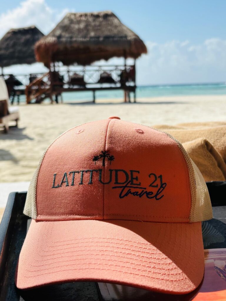 Latitude 21 Travel baseball cap resting on soft beach sand at El Dorado Maroma adult-only resort