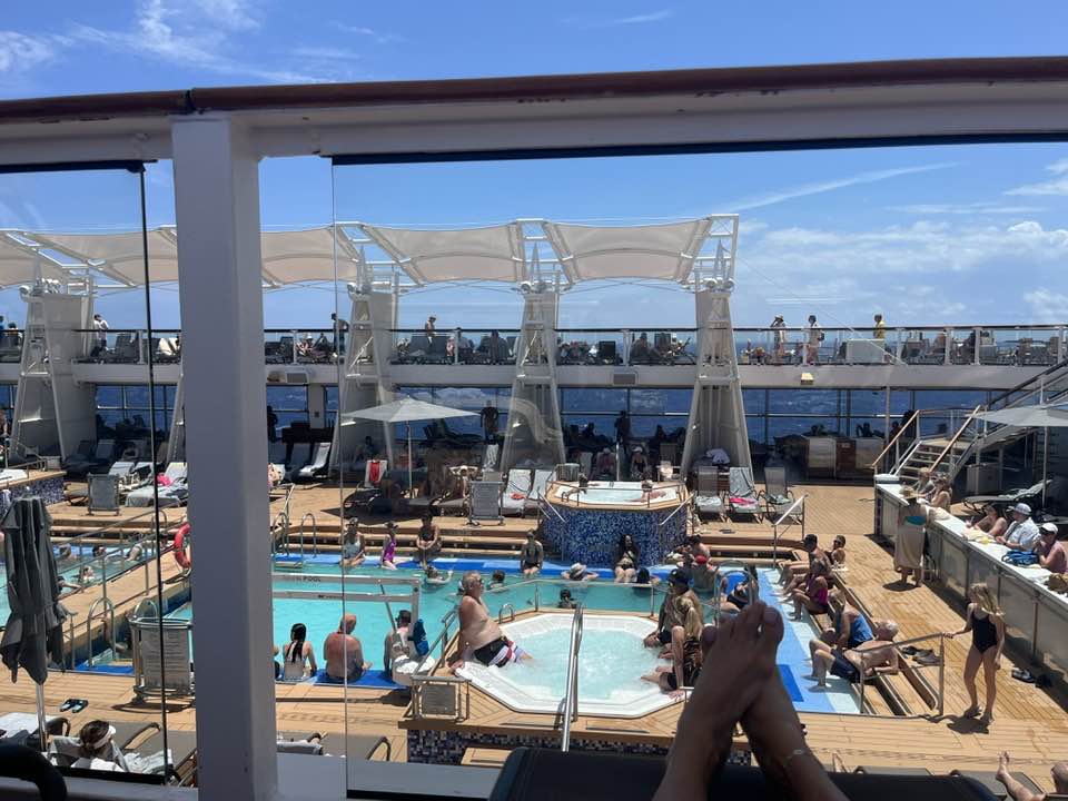 Celebrity Eclipse main pool deck on a sea day, with sun loungers, swimming pool, and guests across two decks viewed from a deck chair