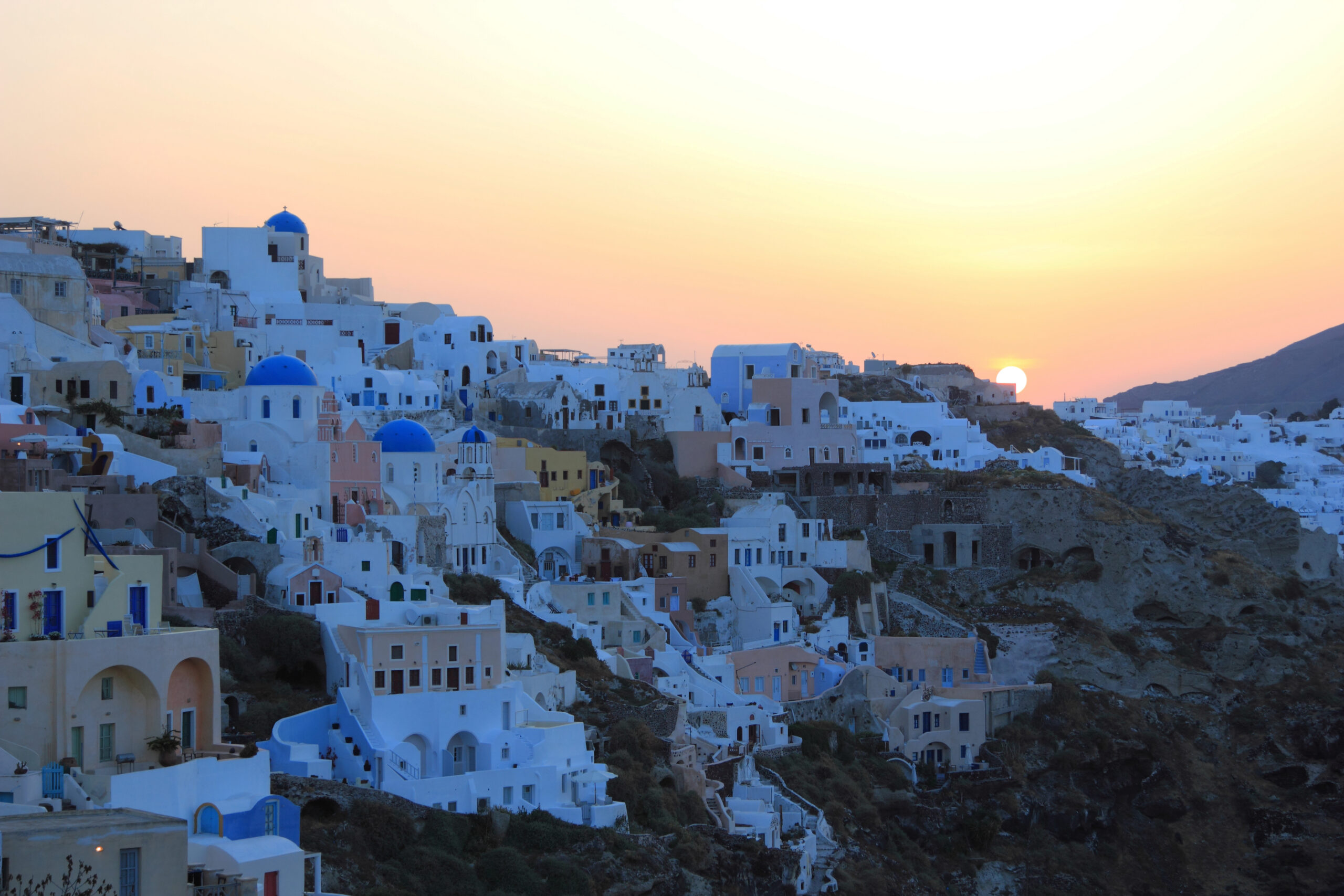 Whitewashed cave houses and blue-domed churches of Oia village at sunset on the Santorini caldera in Greece