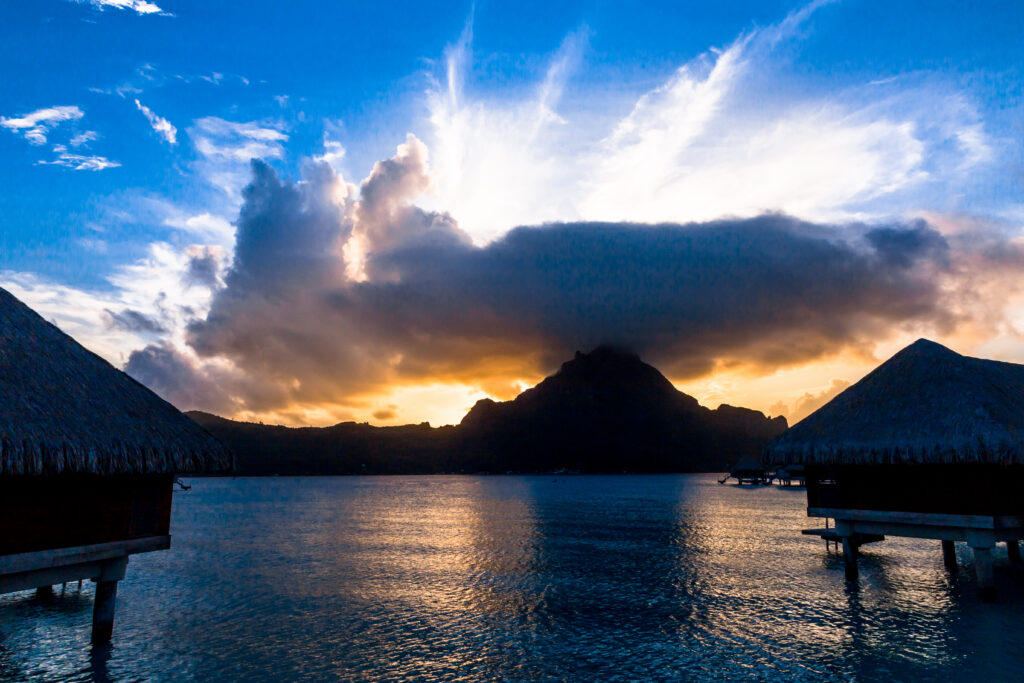 Glowing tropical sunset with sunbeams breaking through clouds above a still lagoon