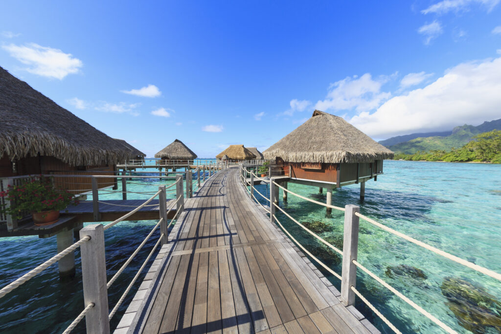 Wooden boardwalk leading across a turquoise lagoon to thatched overwater bungalows