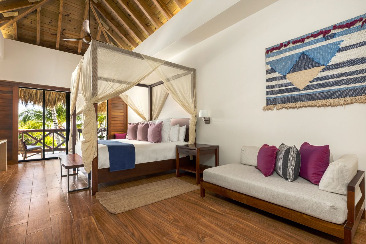 Preferred Club bungalow suite at Secrets Cap Cana with a thatched vaulted ceiling, four poster bed and a balcony over the palms