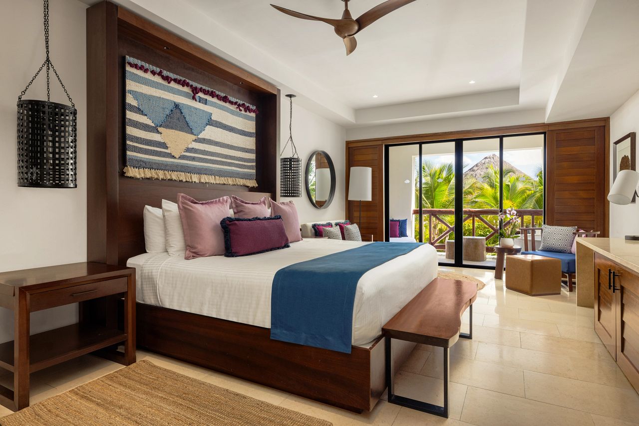 Tropical view Junior Suite at Secrets Cap Cana with a furnished balcony looking onto palms and a thatched palapa roof