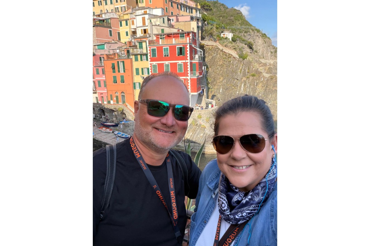 Sarah and John in front of colorful houses in Cinque Terre on the Italian Riviera during a Mediterranean cruise